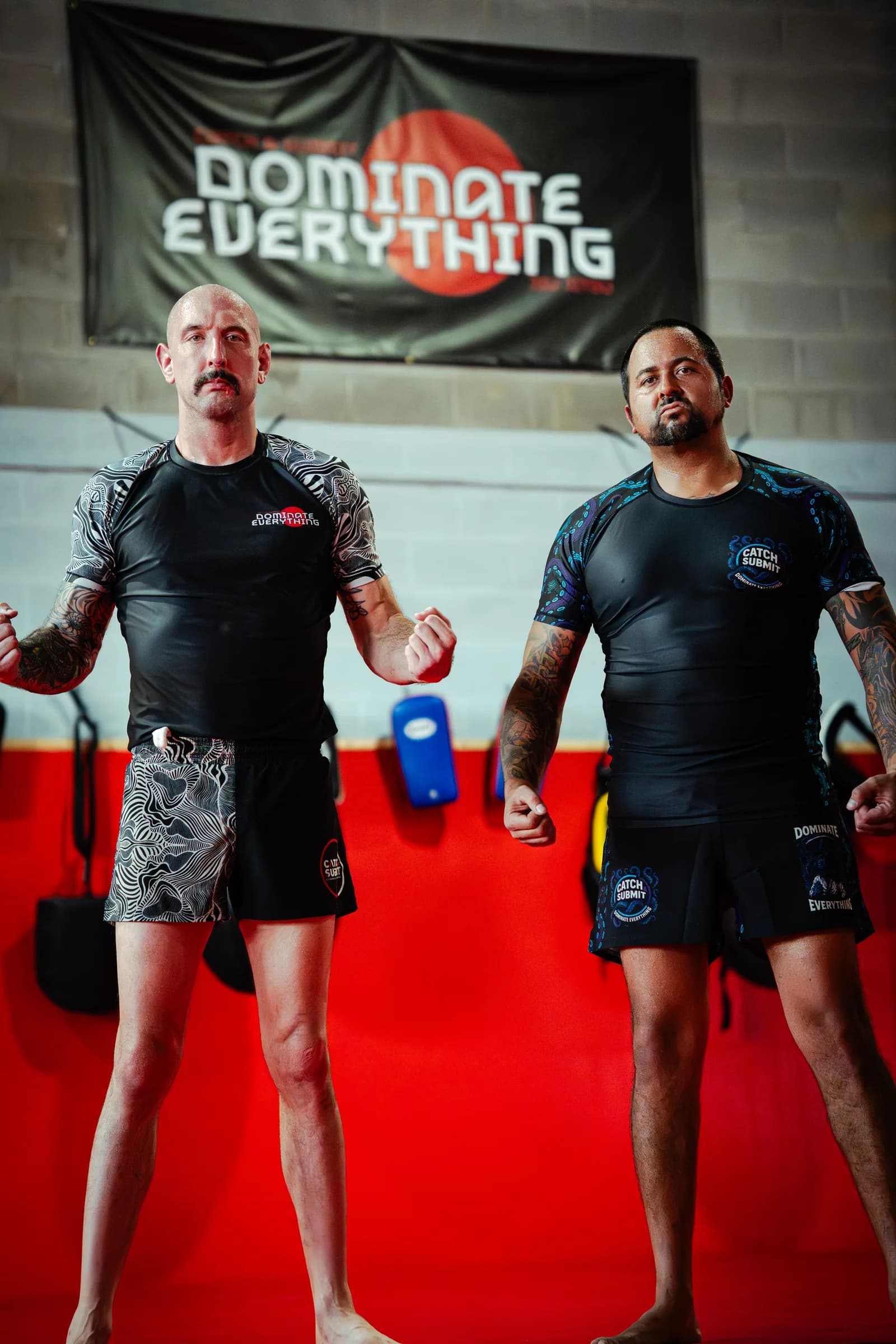 Two athletes in Catch & Submit gear under the Dominate Everything banner