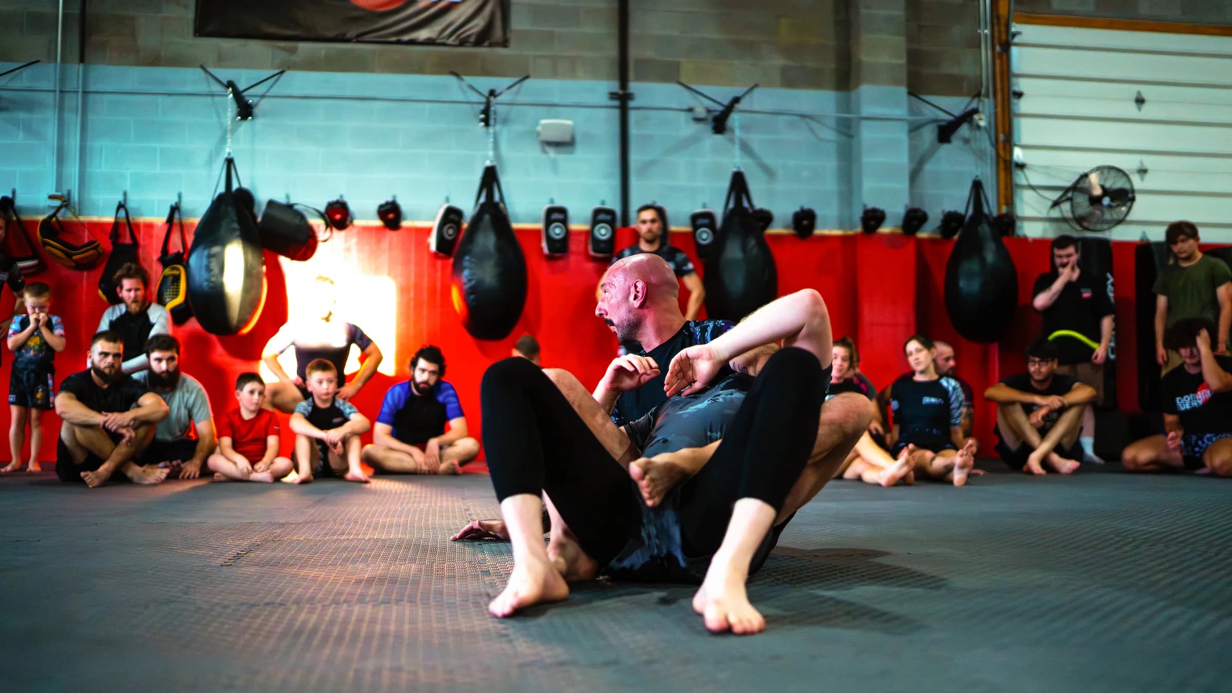 A coach demonstrating a guard position on the mats while a class watches